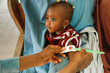 Closeup of a health worker's hand with a malnutrition measuring band circling the arm of a baby girl with big eyes. Photo: WFP/Nommiyid Chantu